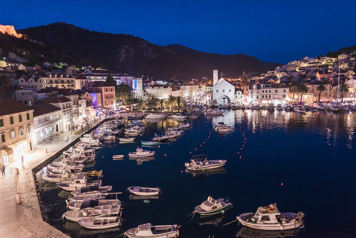 The marina in Hvar, Croatia at night showing bright lights from the town and mountains in the background