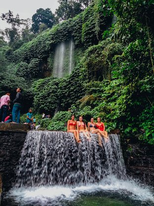 Girls sat on waterfall with green trees behind, Lombok Indonesia