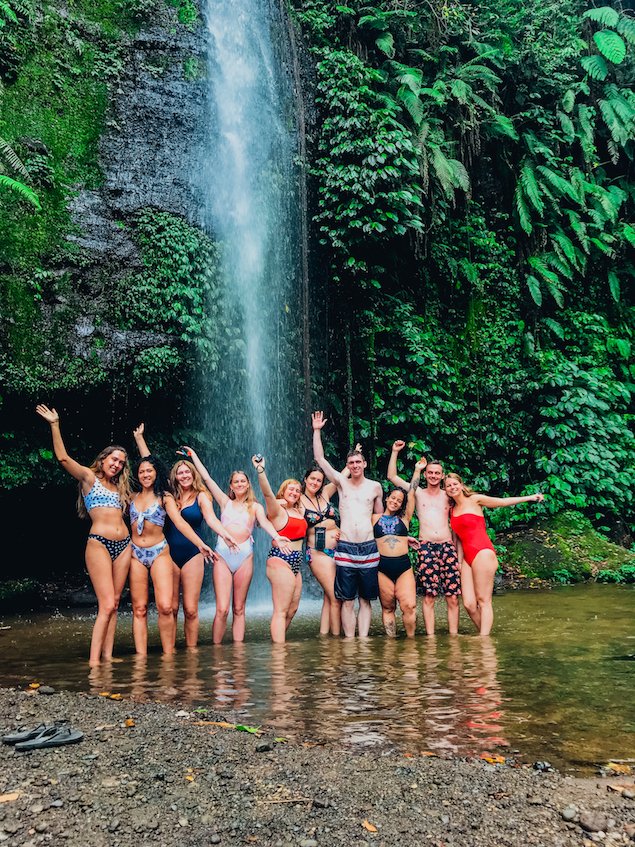 Group of travellers stood under waterfall with jungles behind