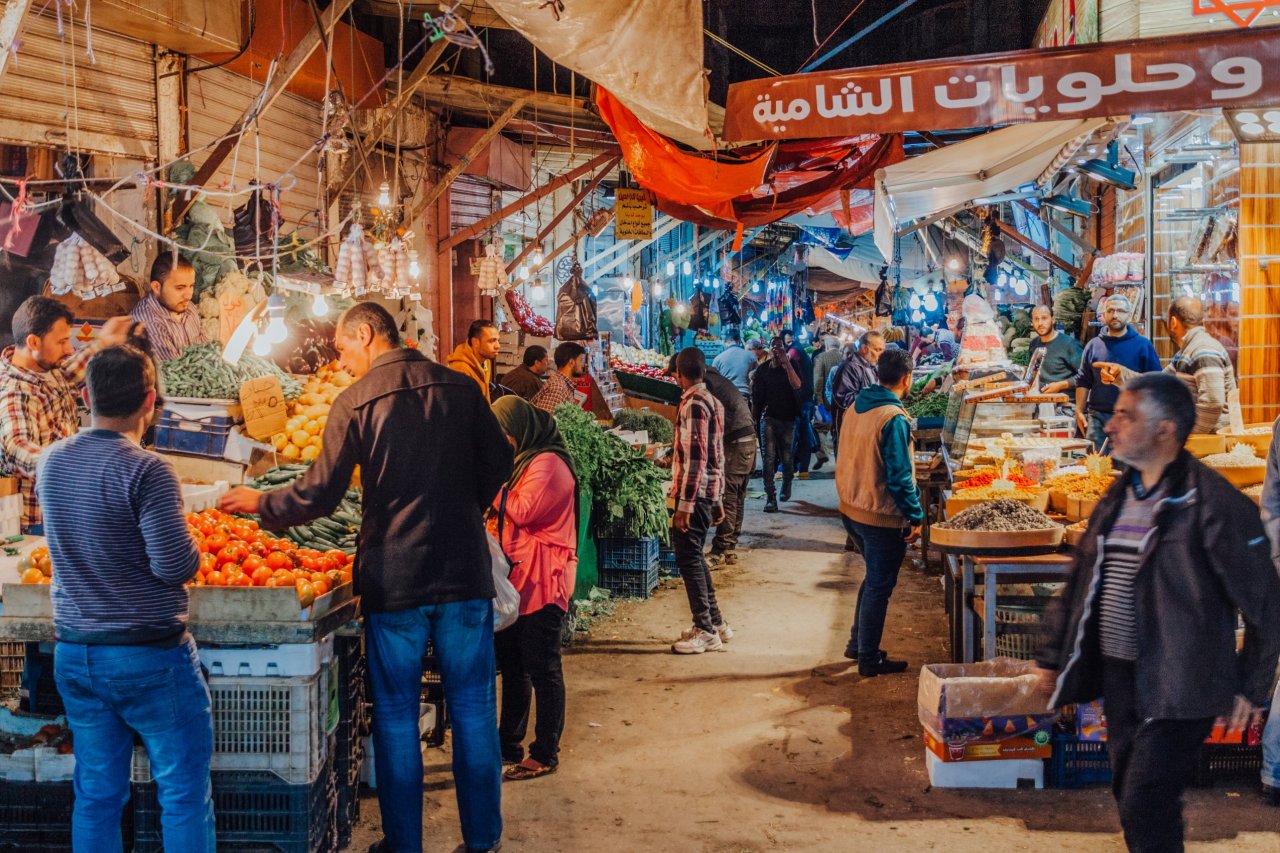 A bustling market street in Amman Jordan. On the left there is a vegetable stall and on the right there is a confectionary stall