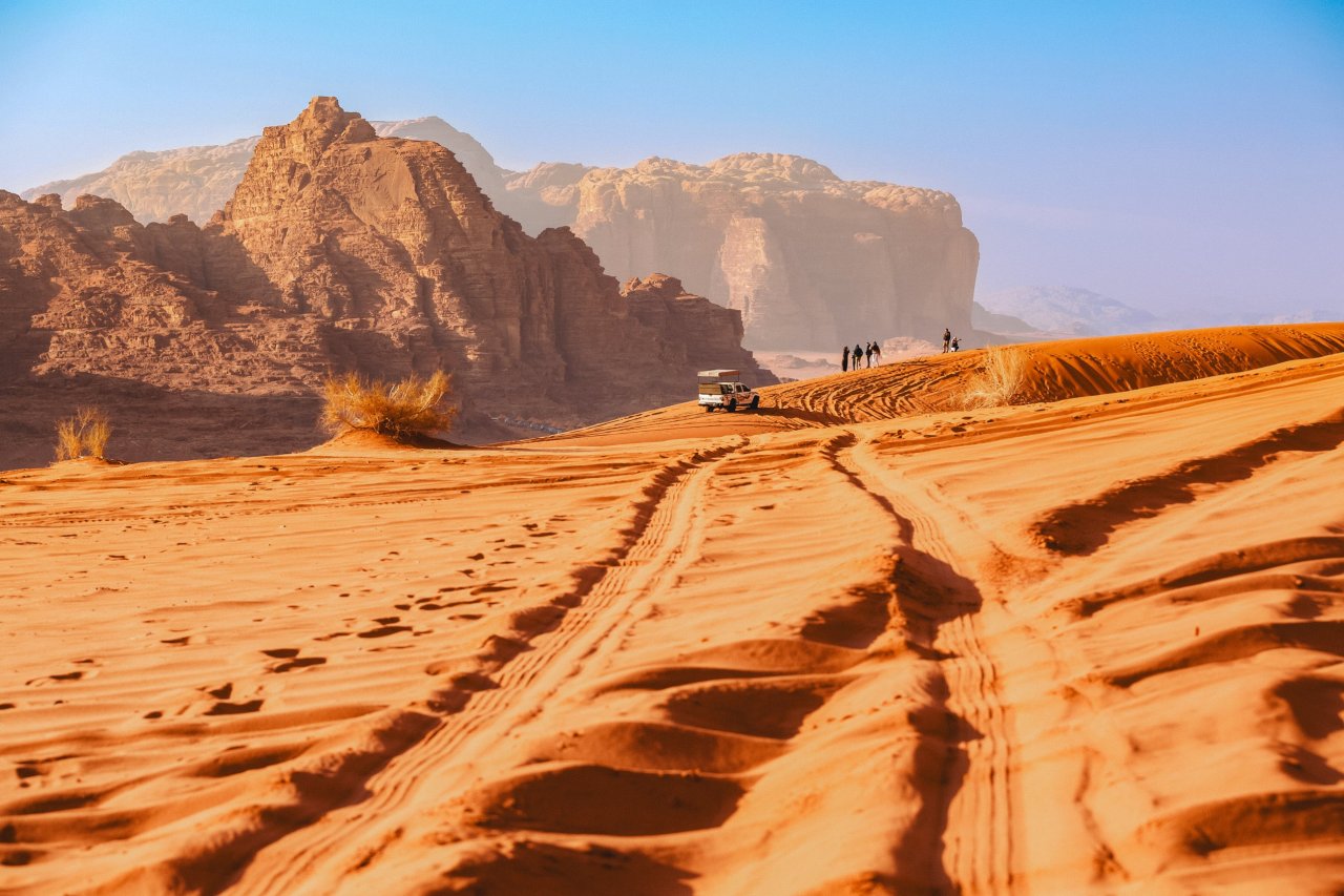 An amazing photo of the Wadi Rum desert in Jordan with a group in the distance and tyre marks in the centre of the dunes
