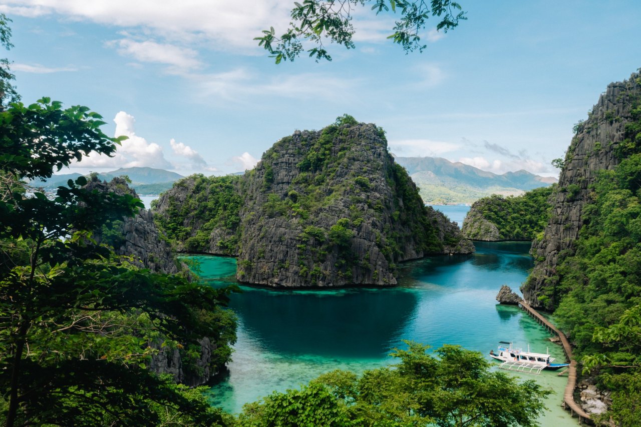 Panoramic view of the iconic Kayangan Lake viewpoint in Coron, Palawan, with turquoise water, limestone karsts, and a traditional Filipino boat.