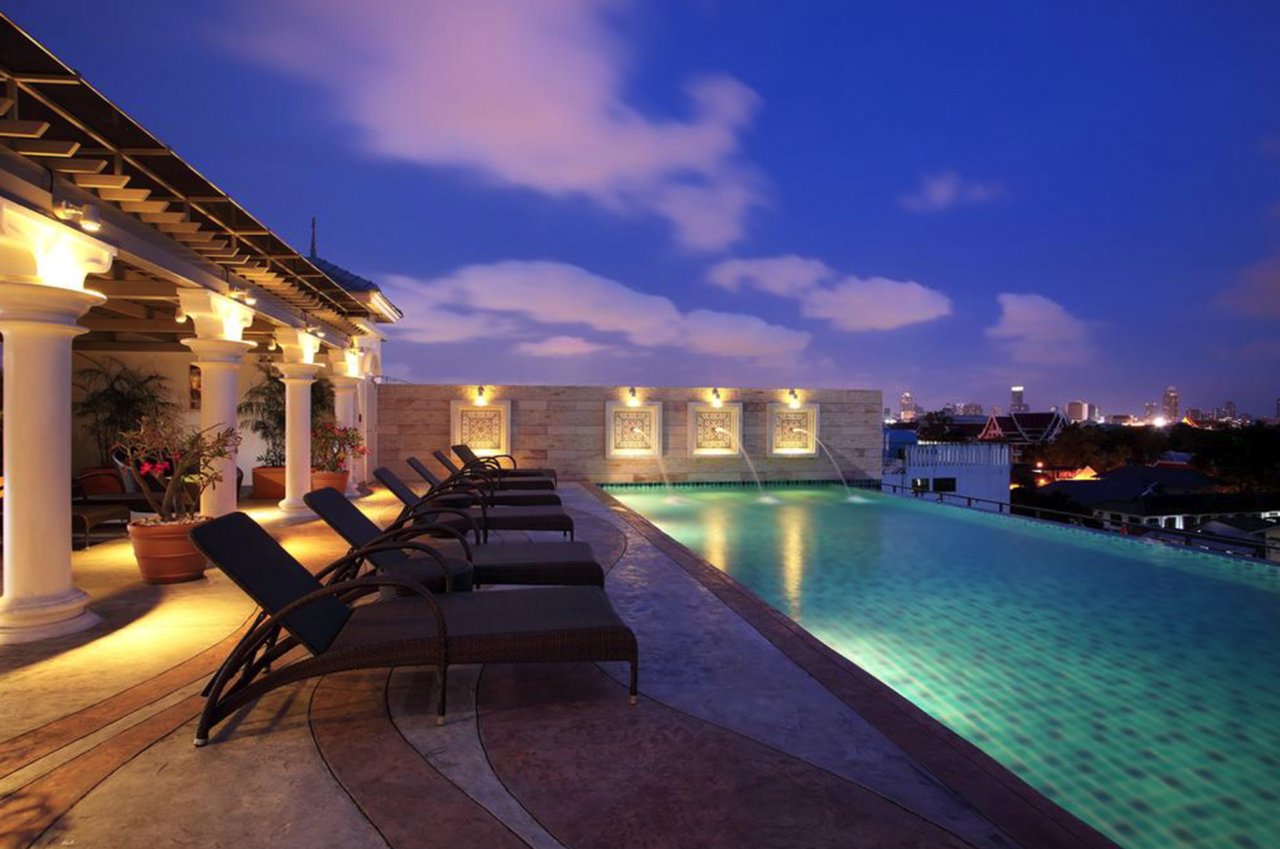 A shot of the hotel in Bangkok's rooftop pool with the pool lights on, surrounding sun loungers at twilight in Thailand.. 