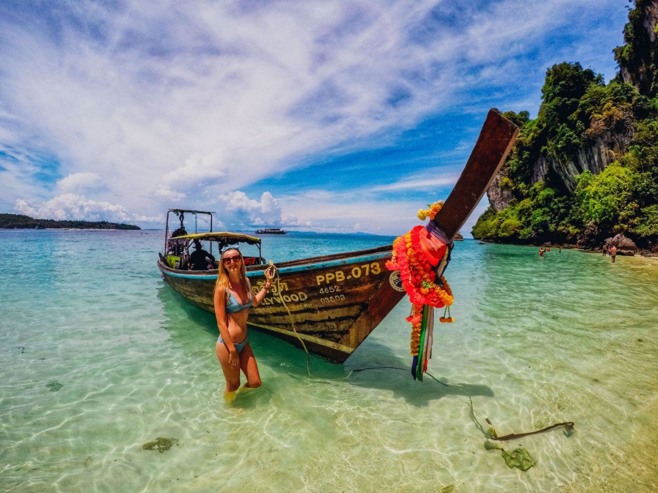 Girl standing next to a longtail boat in the ocean with blue sky